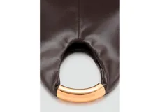 Bolso de mano tipo hobo, confeccionado en poliuretano color marrón oscuro con acabado liso. Presenta un diseño minimalista con una estructura rígida y un asa superior metálica en tono dorado.