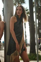 Vestido corto negro con lentejuelas, escote halter y detalle de flecos dorados en el lateral.