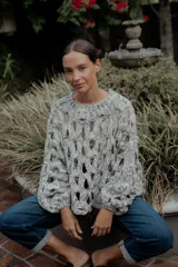 Buzo de tejido de punto calado con diseño de red, cuello redondo y mangas largas abullonadas. Presenta una textura jaspeada en tonos gris y blanco.