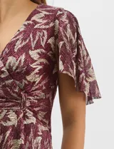 Vestido largo de fiesta con diseño cruzado, escote en V y drapeado lateral en la cintura. Presenta mangas cortas acampanadas y falda amplia con caída fluida. Confeccionado en tejido liviano con acabado plisado y estampado floral metalizado.