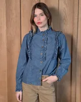 Camisa de denim 100% algodón, de color azul, con cuello alto con volados, botonadura frontal y detalles de volados en los hombros. Cuenta con mangas largas terminadas en puños con volados.