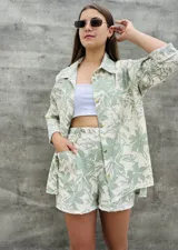 Conjunto de camisa y short con estampado de hojas en tonos verde y blanco. La camisa es de manga larga con botones y el short es de tiro alto con bolsillos laterales.