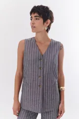 Chaleco largo color blanco con rayas verticales finas color beige, con cuello en V y cierre frontal con botones marrones. Incluye pañuelo al cuello con estampado de lunares y rayas.