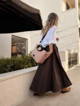 Cartera tipo tote de diseño capitoneado en color marrón claro, con doble asa de mano negra y bolsillos laterales. Presenta un diseño acolchado con líneas verticales en el frente y rombos en los laterales, e incluye una etiqueta decorativa con logo.