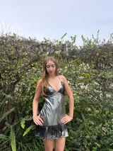 Vestido corto color bordó con escote en V, diseño de top triangular y aberturas laterales en la cintura. Presenta breteles finos cruzados en la espalda y falda con doble volado irregular en el ruedo.