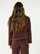 Chaqueta de pana color marrón, con solapas desflecadas, cierre frontal con botones y bolsillos delanteros con solapa desflecada.