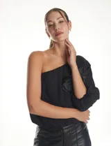 Blusa de un hombro color negro, con diseño asimétrico, una manga larga abullonada, forro interno y apliques de flores de tela en el frente.