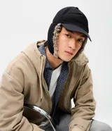 Gorra de estilo aviador con visera curva, confeccionada en poliéster negro. Presenta solapas laterales con forro de piel sintética para cubrir las orejas y ajuste trasero regulable.