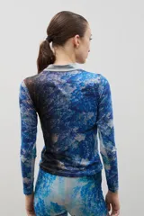 Polera de cuello alto y manga larga, confeccionada en tela sublimada con un estampado artístico que evoca un paisaje boscoso en tonos azules y marrones.
