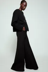 Pantalón de tiro alto con diseño flare, confeccionado en tela de color negro. Presenta cinco bolsillos, cintura con trabillas y cierre frontal con cremallera y botón.