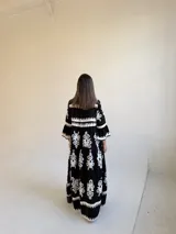 Vestido largo negro con estampado floral blanco, escote en V con cuello mao, cierre frontal de botones y mangas tres cuartos acampanadas.