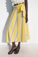 Falda midi tipo pareo de tiro medio, confeccionada en algodón con diseño de rayas verticales en tonos amarillo, gris y blanco. Presenta un bajo asimétrico y cierre lateral con lazada.