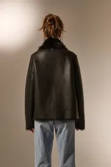 Chaqueta de eco-cuero color beige con interior y cuello de piel sintética al tono. Presenta un diseño holgado, cierre frontal con un botón y solapas amplias.