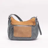 Bandolera de cuero sintético en color celeste con detalles y bolsillo frontal en tono tostado, decorada con tachas metálicas plateadas y cierre superior con cremallera.