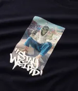 Remera de algodón color negro con cuello redondo y manga corta. Presenta un estampado central con la imagen de un alienígena y la frase 'Stay Weird' en tipografía estilo graffiti.