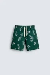 Bañador de hombre largo, color verde oscuro, con estampado de hojas blancas. Presenta cintura ajustable con cordón beige y forro interior.