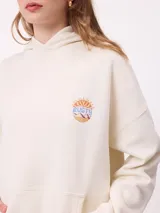 Canguro color crema con capucha y estampado grande en la espalda de un sol con un ojo, montañas, mariposas y texto.