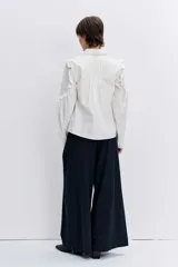 Camisa de color azul oscuro, con cuello clásico, cierre frontal de botones y detalle de volados en los hombros y a lo largo de las mangas largas.