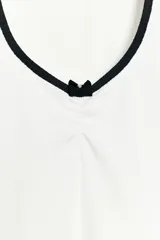 Camiseta blanca de manga corta y corte slim fit, con escote redondo ribeteado en negro, detalle de frunce en el centro del pecho y un pequeño lazo negro decorativo.