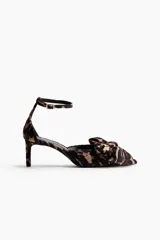 Zapato de tacón fino con pulsera ajustable al tobillo, confeccionado en velour con estampado animal print. Presenta una moña decorativa en la punta fina y forro interior de satén.