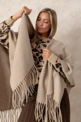 Ruana abierta de color beige, confeccionada en tejido de punto con terminación de flecos en el ruedo.