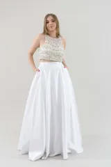 Vestido de fiesta blanco de dos piezas. Top corto con escote halter, bordado con perlas y strass. Falda larga de piel de ángel con bolsillos y pretina alta.