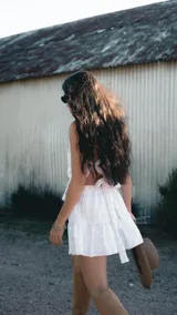 Falda corta de color blanco con tejido bordado y sutil brillo plateado. Presenta un diseño con volado en el ruedo, corte evasé y caída liviana.