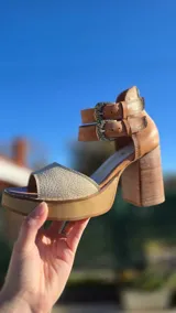 Sandalias de cuero color suela y beige, con plataforma de madera, taco ancho y doble tira con hebillas metálicas en el tobillo. Cuentan con cierre trasero.