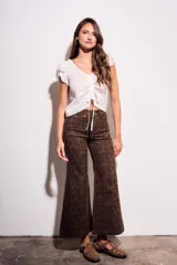 Pantalón de jean tiro medio, corte wide leg acampanado, color marrón oscuro con estampado animal print en tonos más oscuros y pequeños puntos rosados.