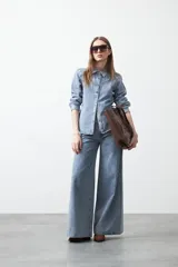 Camisa de jean color azul claro con tachas metálicas en el canesú y a lo largo de las costuras frontales. Tiene mangas largas con puños abullonados y cierre frontal con botones.