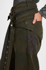 Jean tipo baggy de pierna ancha y recta, color marrón oscuro. Presenta detalles de costuras decorativas, bolsillos laterales redondeados y bolsillos traseros grandes. Incluye tiras ajustables con hebillas metálicas en los tobillos para un efecto fruncido.