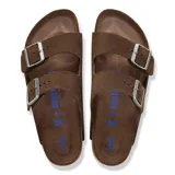 Sandalias Birkenstock modelo Arizona de dos correas ajustables con hebillas metálicas. Presentan una capellada de gamuza marrón, plantilla anatómica de corcho y suela de goma antideslizante.
