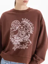 Buzo de cuello redondo color marrón, con diseño gráfico estampado en color blanco en el frente que incluye elementos como un símbolo de paz, una figura central y la palabra 'paix'. Presenta un corte holgado con mangas largas y puños acanalados.