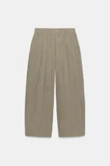 Pantalón fluido de tiro medio color verde militar, con cintura elástica en la parte trasera, pinzas en el delantero y bolsillos laterales ocultos en la costura. Presenta un diseño de pernera ancha y corte tobillero, con cierre frontal de cremallera y botón.