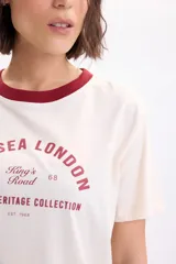 Remera manga corta de color crudo, con cuello redondo en tono bordó y estampa frontal con texto en el pecho.