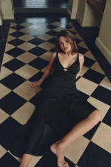 Vestido largo de satén negro, con escote en pico, tirantes finos dobles, abertura en la espalda y bajo asimétrico. Cierre lateral con cremallera oculta.