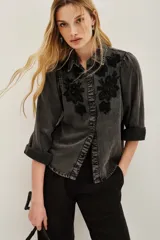 Camisa de liocel color gris oscuro, con cuello clásico y botones frontales. Presenta bordados florales en negro en la parte delantera y mangas abullonadas con puños doblados.