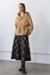 Cazadora tipo anorak color beige, con capucha ajustable, manga larga y bolsillo frontal de plastrón con solapa. Cuenta con cordones elásticos ajustables en la cintura y el bajo, y cierre frontal con botones a presión.