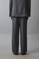 Pantalón de traje con corte flare fit, confeccionado en tejido con lana. Presenta diseño de tiro medio con pinzas frontales, bolsillos laterales y bolsillos traseros de vivo. Cierre frontal con cremallera y botón.