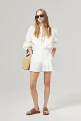 Short de lino blanco con cintura alta, tablas, bolsillos laterales y cierre frontal con gancho metálico.