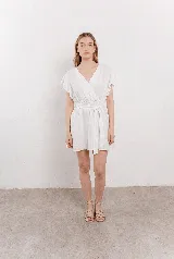 Vestido corto de lino blanco con escote cruzado en V, mangas cortas con vuelo y cintura elastizada con lazo para ajustar la silueta.