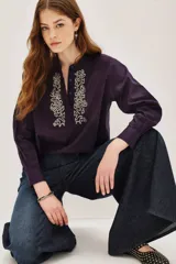 Camisa de algodón color violeta oscuro, con cuello mao, cierre frontal parcial con botones y detalle de bordado decorativo en el frente. Posee mangas largas con puños abotonados.