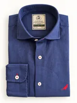 Camisa de lino color azul, de corte slim fit, con cuello italiano, manga larga y botones blancos con costuras rojas. Presenta un bordado de ave en color rojo en la parte inferior.