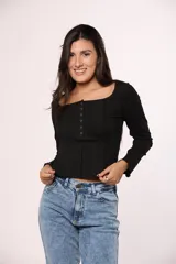 Remera manga larga de tela acanalada color negro, con escote cuadrado y cierre frontal con botones decorativos. Presenta costuras verticales visibles y corte ajustado.