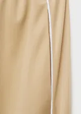 Pantalon de corte recto y tiro medio en color beige, con detalle de rayas laterales verticales en contraste blanco. Cuenta con cintura elástica y bolsillos laterales.