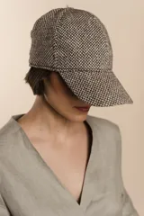 Gorra con visera confeccionada en lana fina sin teñir, con un sutil patrón de tejido en espiga.