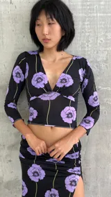 Top de lycra con escote en V profundo y mangas tres cuartos. Presenta un diseño estampado de flores violetas sobre fondo negro con líneas verticales finas en color amarillo.