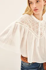Camisa blanca de corte amplio y diseño cropped, confeccionada en algodón con detalles de encaje bordado en la parte superior y mangas acampanadas con textura rayada.