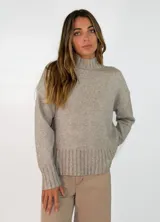 Sweater de punto color beige con cuello alto, mangas largas y puños y ruedo acanalados.