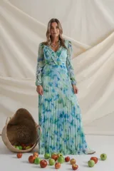 Vestido largo de gasa plisada con estampado floral en tonos celeste, verde y azul. Tiene escote cruzado con detalle de alforzas, mangas largas con abertura y falda plisada. Ideal para eventos de día.